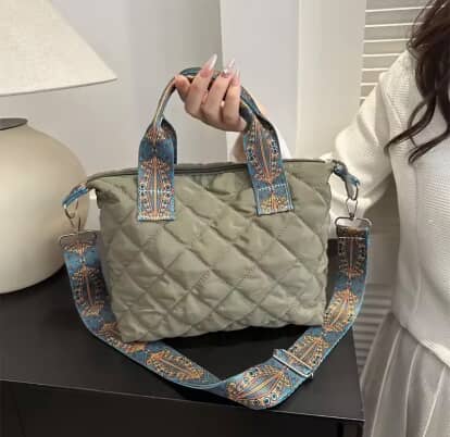 Person holding a green quilted handbag with decorative straps in a room setting.